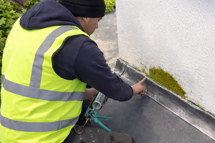 roofer applying sealant to led flashing on flat roof