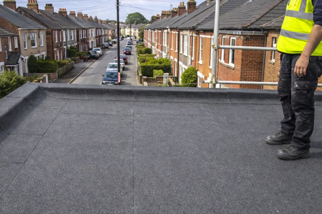 roofer on a flat garage roof inspecting a leak